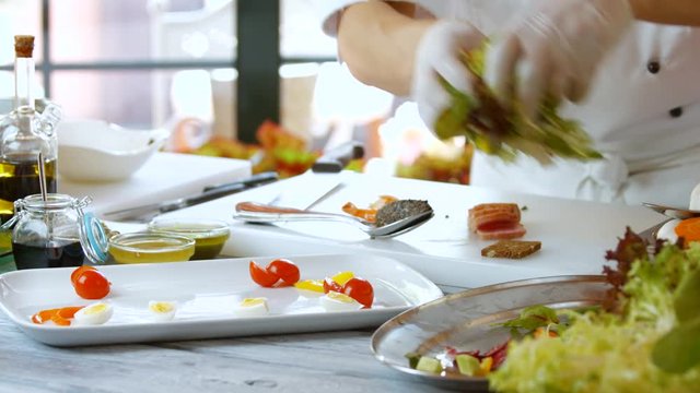 Hands put salad on plate. Sliced eggs and small tomatoes. Salad with frisee lettuce. Only fresh herbs.