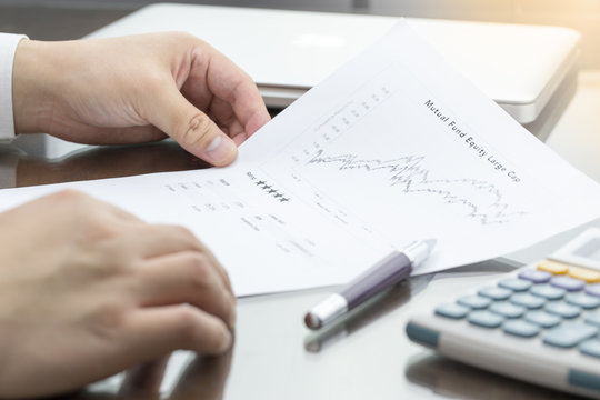 Businessman or fund manager review Mutual Fund information with performance line graph and benchmark with pen, calculator and computer laptop.