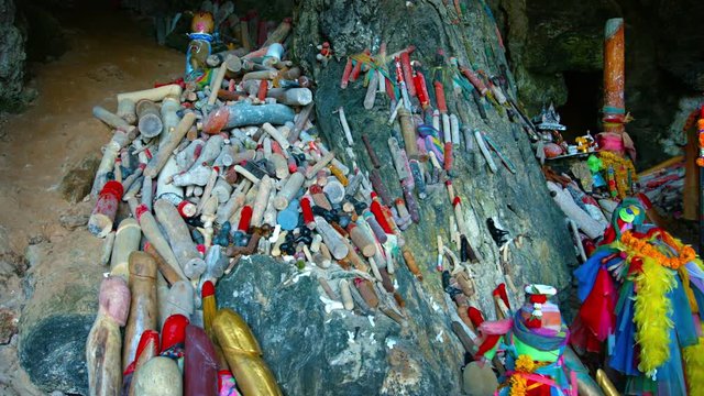 Video UHD - Heaps of colorfully painted, wooden penises, piled on the rocks as an offering for a Buddhist shrine, inside a cave in Thailand.