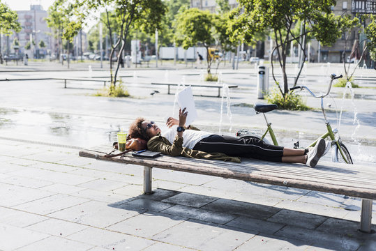 Young woman lying on a bench reading notes