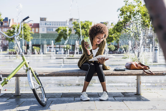 Young woman sitting on a bench with beverage reading notes