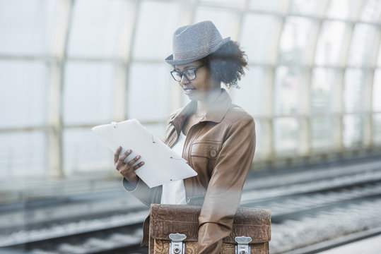 Young woman with briefcase and file reading while waiting at platform