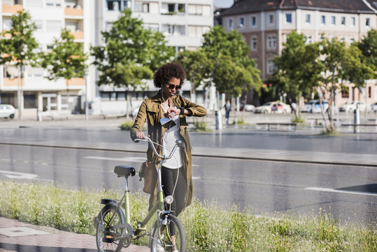 Young woman with with bicycle checking the time