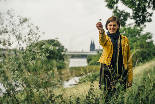 Germany, Cologne, happy woman standing on a meadow showing plant