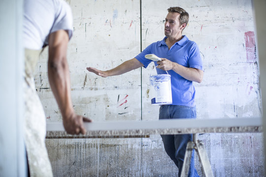 Man talking to colleague while holding bucket of paint in canvas workshop