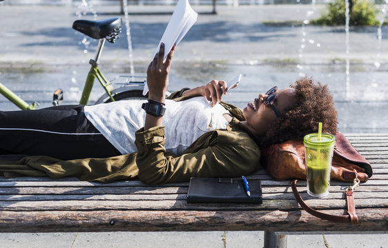 Smiling woman lying on a bench reading notes
