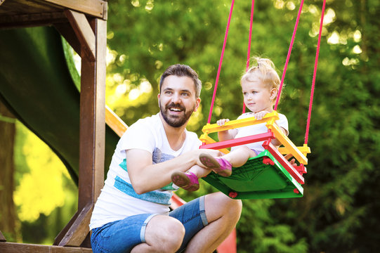 Portrait of happy father with his little daughter sitting on a swing of playground