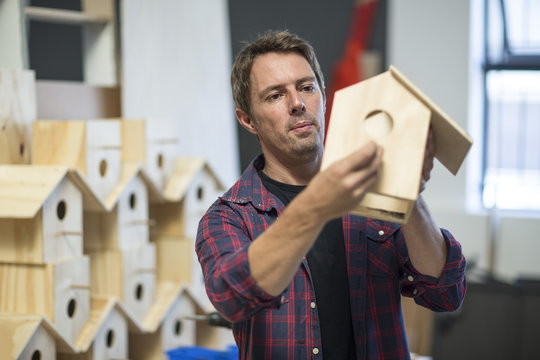 Man holding unfinished birdhouse in workshop