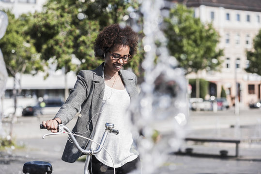 Portrait of smiling woman with bicycle listening music with earphones