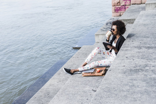 Young businesswoman with digital tablet drinking coffee to go at riverside