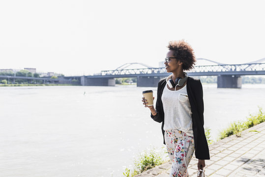 Germany, Mannheim, young businesswoman with coffee to go walking at riverside
