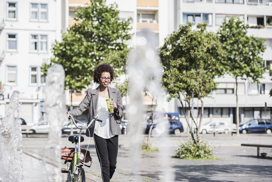 Portrait of smiling woman with bicycle listening music with earphones