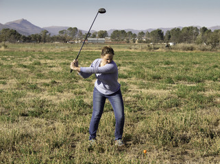 Young woman practicing golf in rough rural field