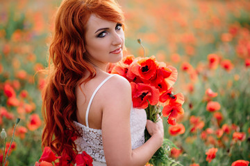 Naklejka premium beautiful young red-haired woman in poppy field holding a bouquet of poppies