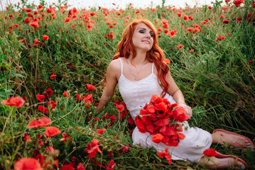 beautiful young red-haired woman in poppy field holding a bouquet of poppies