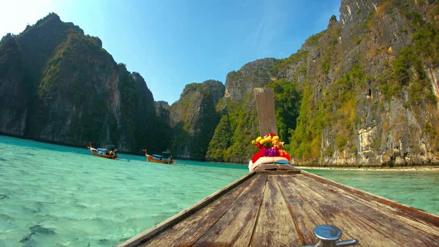 Video 4k - Onboard perspective of Phi-Phi Island's crystal clear waters and towering seacliffs from the weather worn deck of a motorized longtail boat in southern Thailand.