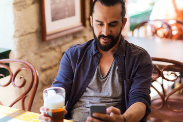 man with smartphone drinking beer at bar or pub