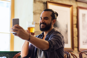 man with smartphone drinking beer at bar or pub