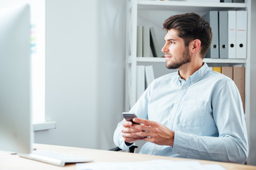 Businessman sitting at his workplace in office with mobile phone