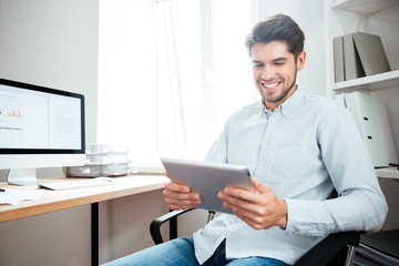 Smiling businessman sitting and using tablet computer in office