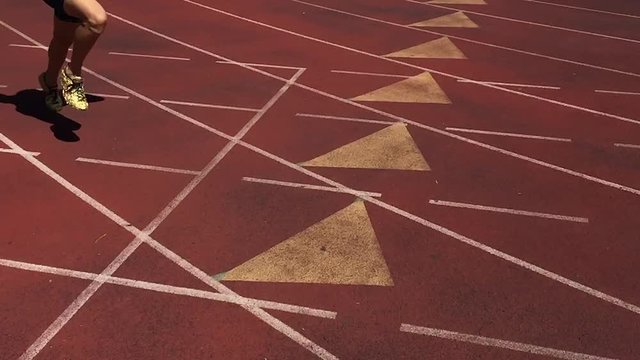 Athlete in gold shoes sprinting in slow motion on rustic red running track