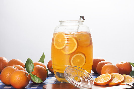 A jug of orange lemonade with fresh oranges.