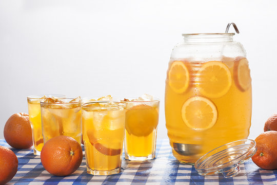A jug and glasses of orange lemonade with fresh oranges.