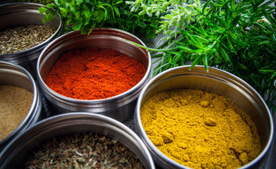 Spices in metal containers and fresh herbs on wooden table