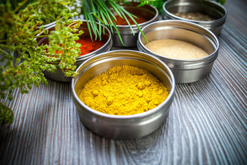 Spices in metal containers and fresh herbs on wooden table