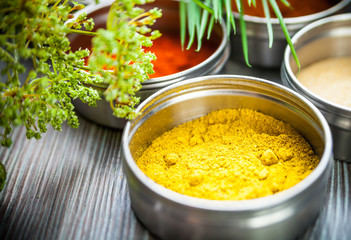 Spices in metal containers and fresh herbs on wooden table