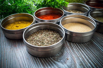 Spices in metal containers and fresh herbs on wooden table