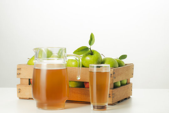 Pitcher and glass of apple juice and fresh apples in a wooden box.