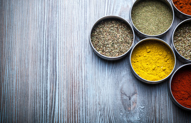 Spices and herbs in metal containers on wooden table