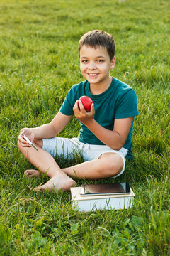 Young boy with a phone and apple on the grass