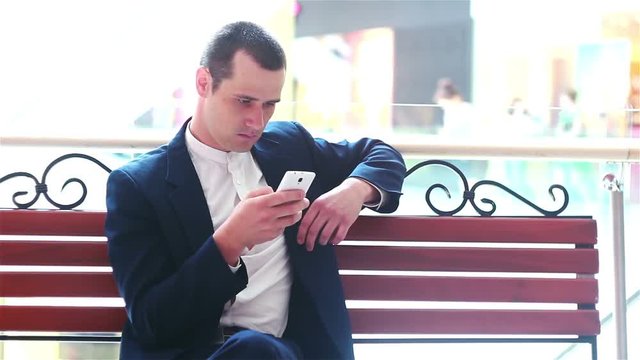 young businessman is resting sitting on a bench looking at smartphone