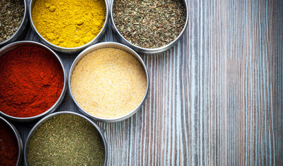 Spices and herbs in metal containers on wooden table