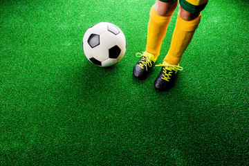 Unrecognizable little football player against green grass, studi