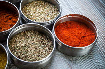 Spices and herbs in metal containers on wooden table
