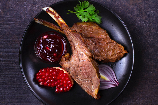 Grilled rack of lamb with pomegranate sauce in black plate on dark textural background. View from above, top studio shot