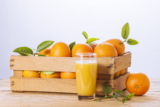 Oranges with leaves in a wooden box and orange juice.