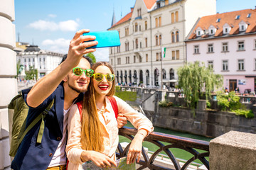 Young couple standing with paper map on the bridge in the center of Ljubljana city. Traveling...