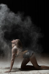 Fototapeta na wymiar Female dancer sprinkle flour on black background