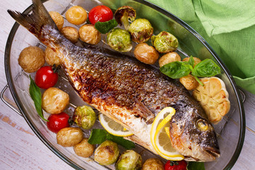 Roasted dorado fish with brussels sprouts, tomatoes, garlic, young potato and greens. View from above, top studio shot
