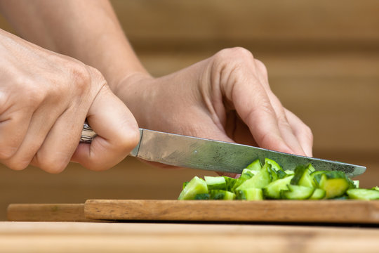 hands slicing cucumber on the wooden cutting board