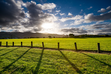 Fototapeta na wymiar Green grass field, wooden Fence and mountain on horizon at summer morning. American spring sunrise in Denver Colorado USA