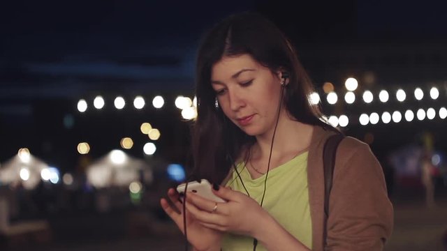 Beautiful girl listening to music on the phone at the fair night close-up