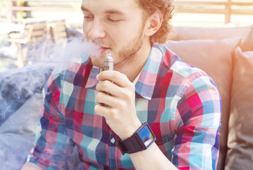 Modern handsome man smoking electronic cigarette in outdoor cafe. Modern lifestyle. Stylish guy outdoor.