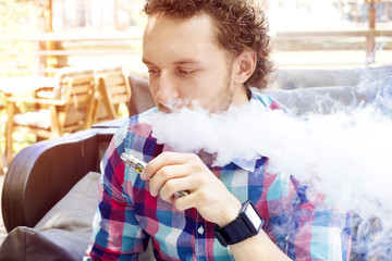 Modern handsome man smoking electronic cigarette in outdoor cafe