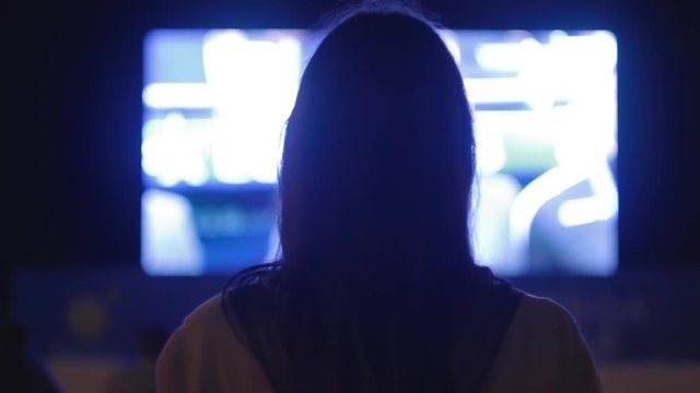  Beautiful girl looking video on the big screen at night close-up
