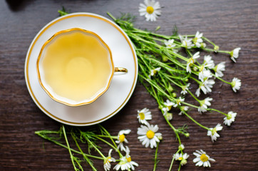 herbal camomile tea in a porcelain cup on a dark wooden background